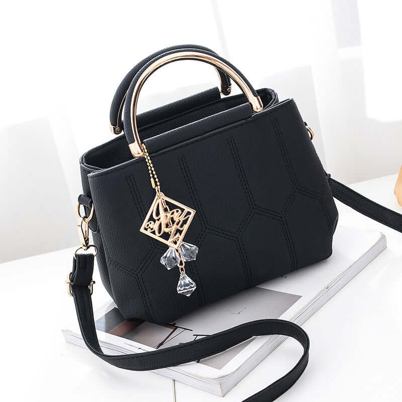 Stylish black shoulder bag with gold handle and decorative charm, perfect for women's fashion and daily use.